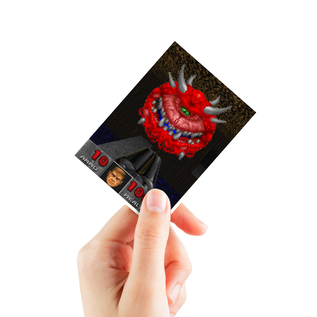 A hand holding a DOOM Cacodemons Apex Deck Protector sleeve featuring a pixelated Cac demon and game HUD elements.