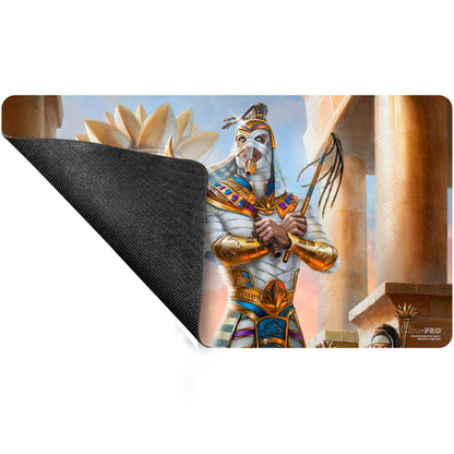 A rectangular playmat featuring artwork of a mummy-like figure in ornate golden armor, holding a whip, with a large lotus flower and ancient pillars in the background. The bottom left corner shows the black textured underside of the mat. Brand: Ultra Pro, Item: Aetherdrift Amonkhet Eternal Might (Commander) Playmat for Magic: The Gathering.