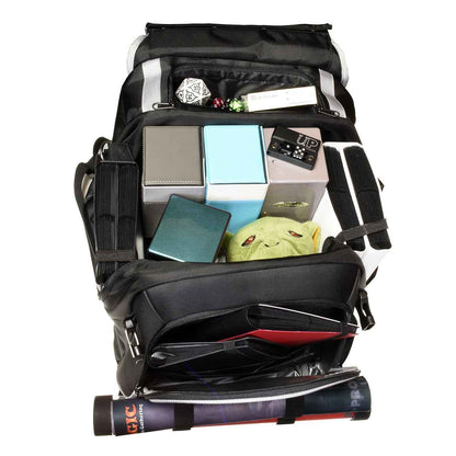 A black backpack with silver trim, filled with various gaming accessories including deck boxes, dice, and a plush toy.